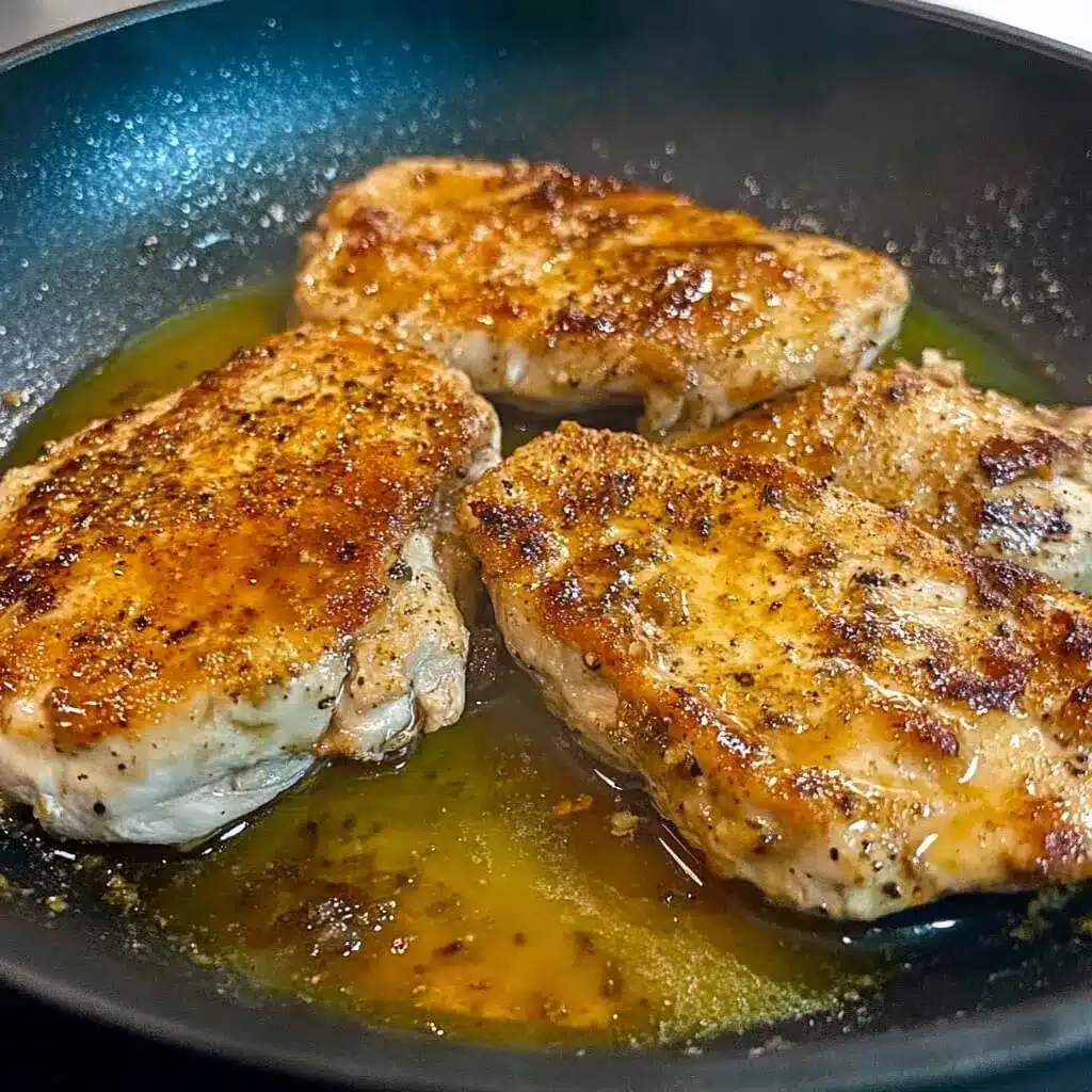 Golden-brown chicken breasts pan-seared in a hot honey glaze, perfect for sandwiches. Chicken breasts cooking in a skillet with seasoned hot honey glaze