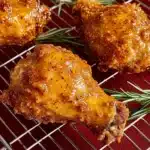 Golden crispy honey butter fried chicken thigh resting on a wire rack with fresh rosemary