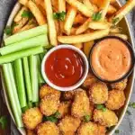 Platter of chicken nuggets and fries with celery sticks, ketchup, and a creamy dipping sauce garnished with fresh parsley.