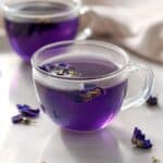 Two cups of freshly brewed butterfly pea flower tea with floating petals