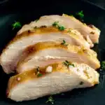 Sliced sous vide chicken breast garnished with fresh herbs and glazed with lemon garlic sauce